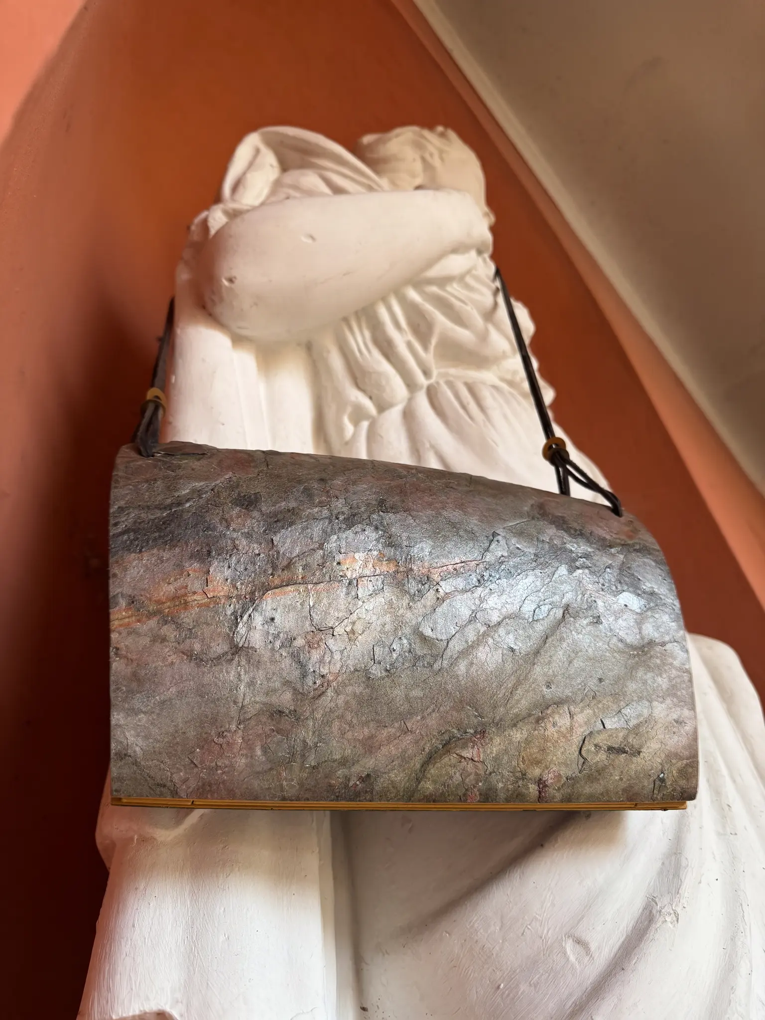 Pyroklast Abendtasche von einer Statue vor orangefarbener Wand getragen